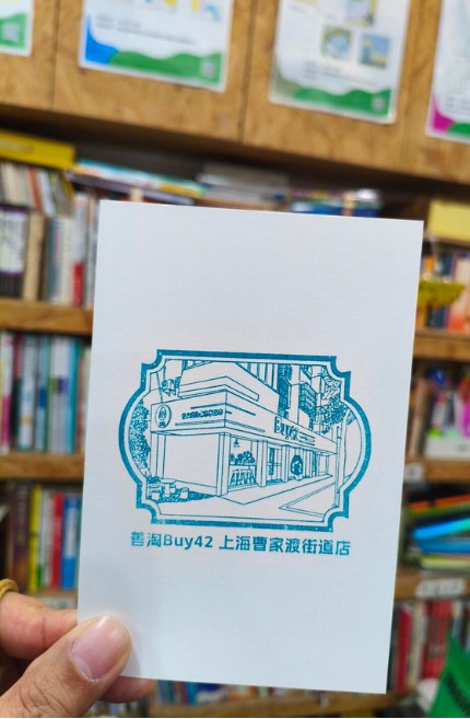 A Shantao Buy42 Shanghai store stamp held in front of bookshelves